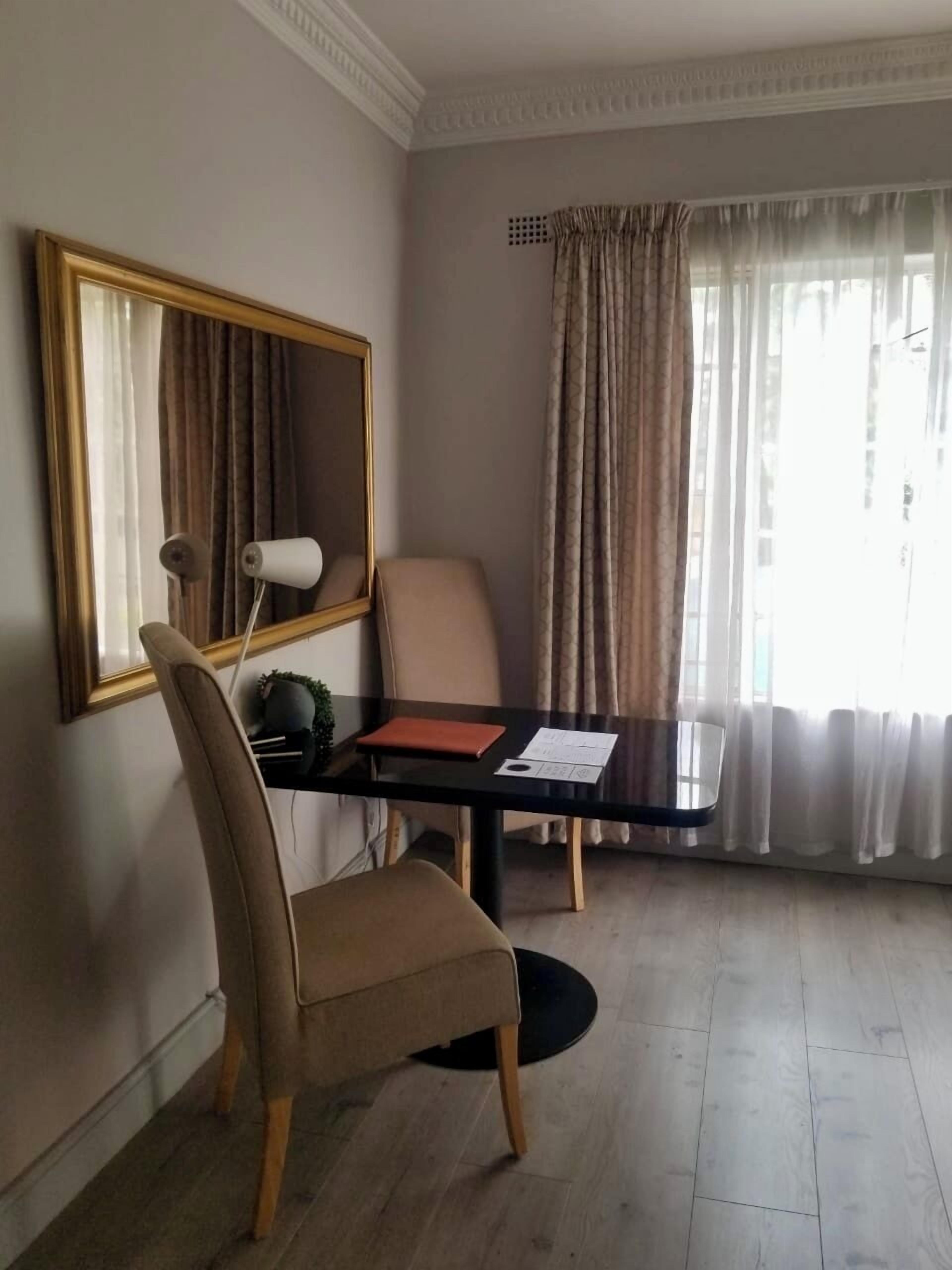 A hotel room with a dining table, a chair, a large mirror, and a window with curtains.