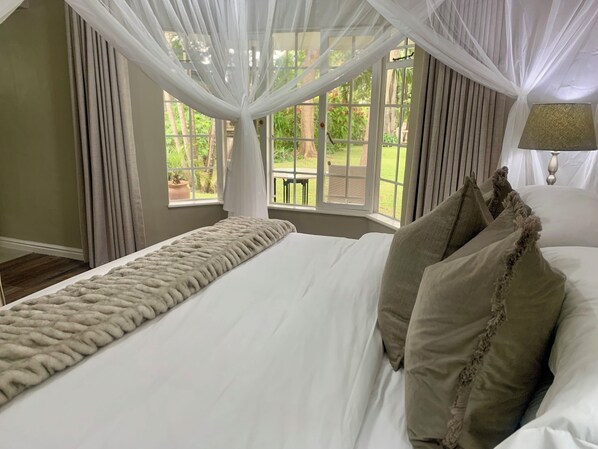 Une chambre à coucher avec un grand lit, un baldaquin et une vue sur un jardin par la fenêtre.