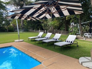 Un área junto a la piscina con sillones de descanso y sombrillas a rayas.