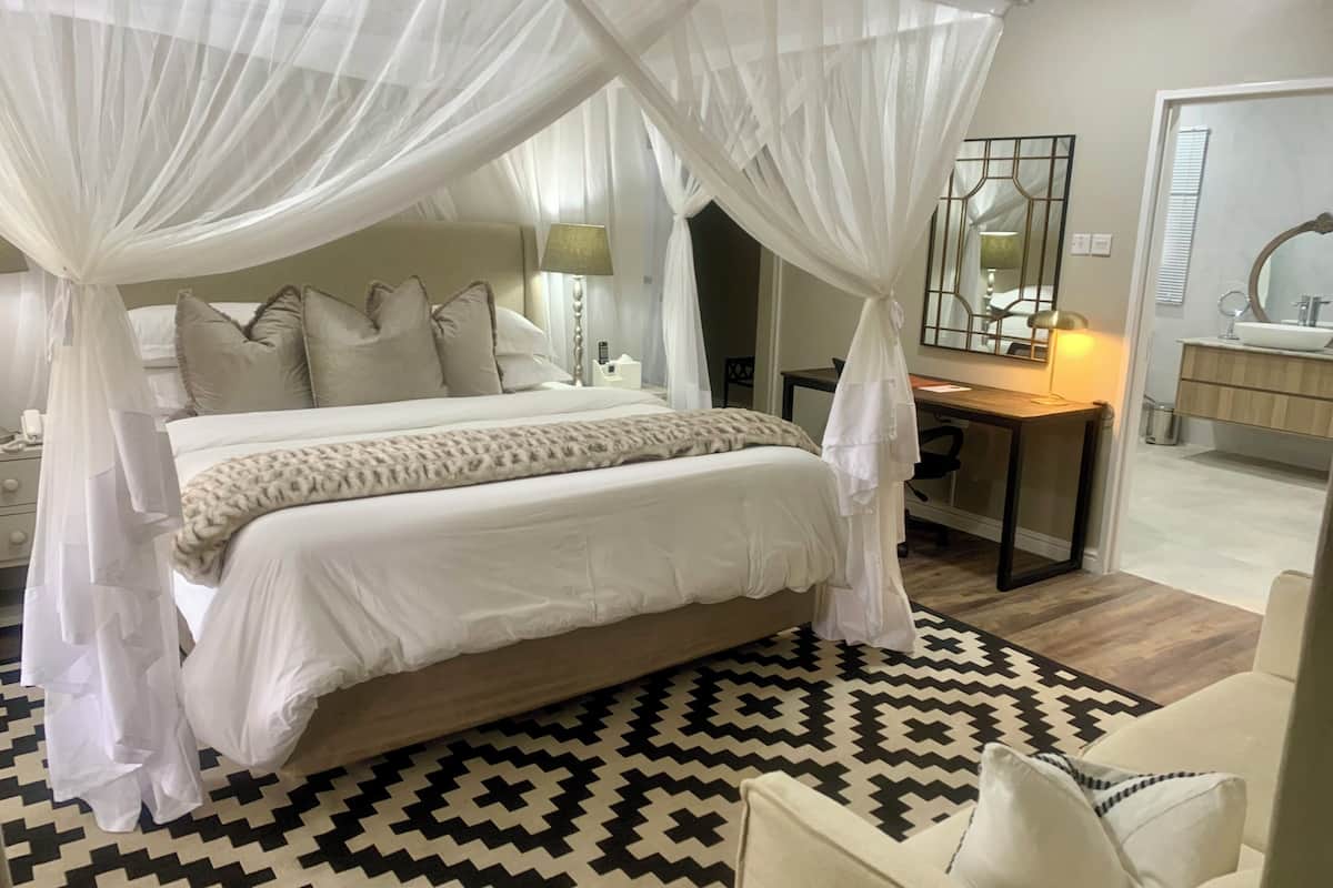 A bedroom with a four-poster canopy bed, a desk, a chair, and a bathroom with a mirror and sink.