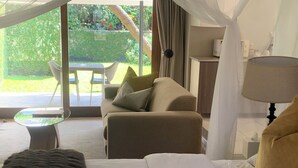 A bedroom with a bed, a sofa, a glass table, and a view of a garden through a glass door. - The Leslie - Bed & Breakfast (Blantyre)