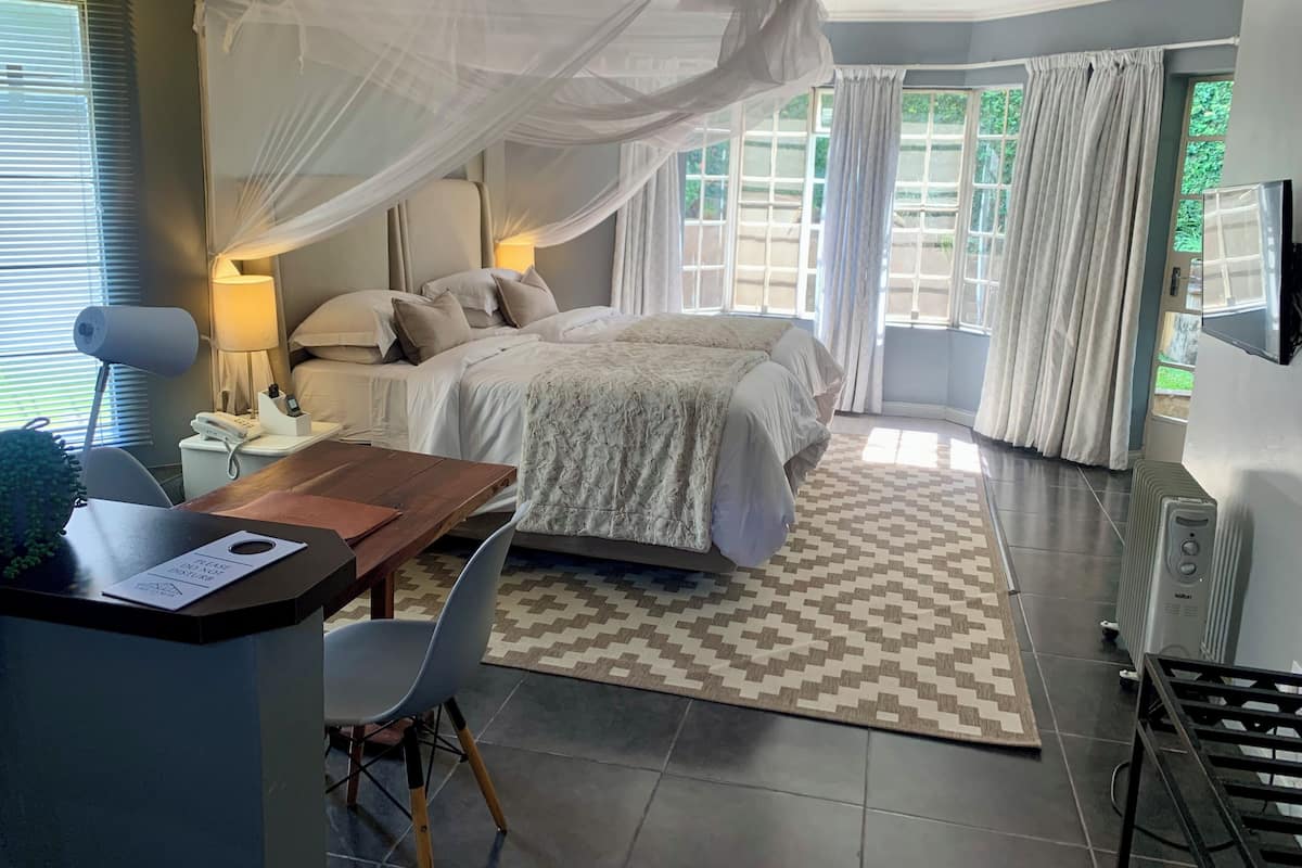 A bedroom with a bed, bedside table, lamp, and a desk with a chair.