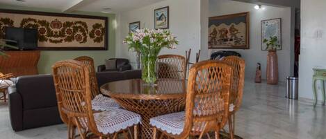 Un coin repas avec une table ronde entourée de chaises en osier, un lustre et un vase rempli de fleurs.