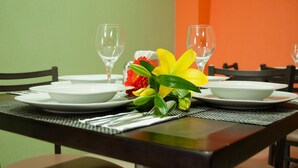 Een eettafel gedekt met witte borden, heldere glazen en een boeket gele en rode bloemen.