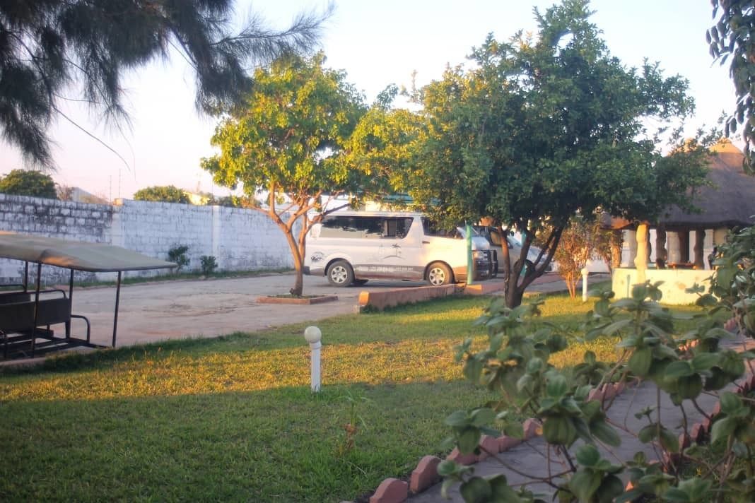Un estacionamiento con un coche blanco, una zona de descanso cubierta y un césped.