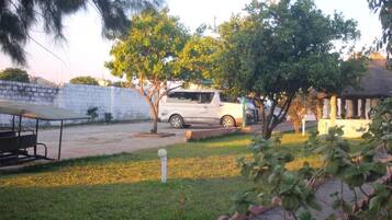 Un estacionamiento con un coche blanco, una zona de descanso cubierta y un césped.