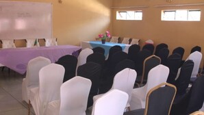 A conference room with rows of chairs, a whiteboard, and a table with a blue tablecloth and flowers. - Nalumba 2 Lodge (Mongu)