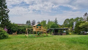 A wooden play structure with a slide and swings in a grassy backyard. - FeWo Walter - House 2 St.- Andreasberg, south-facing slope, quiet, family-friendly, WLAN (St. Andreasberg)