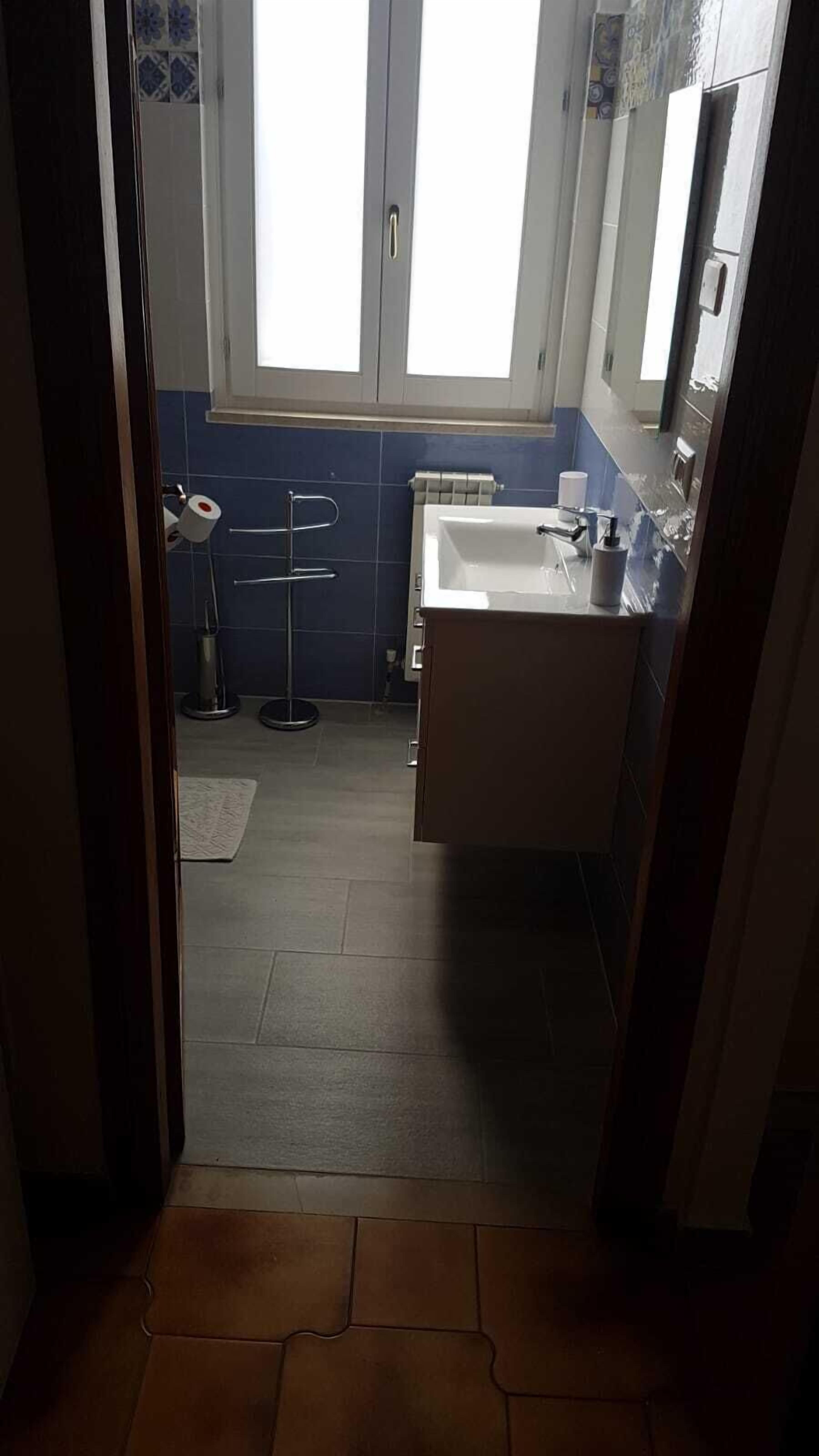 Un couloir étroit mène à une salle de bain équipée d’un lavabo, de toilettes et d’un porte-serviettes.