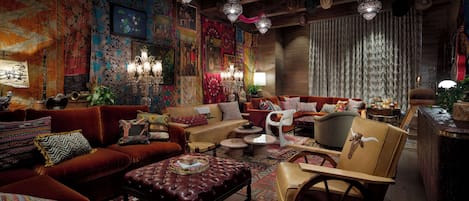 A cozy, eclectic living room with a mix of vintage and modern furniture, including a red sofa, a patterned ottoman, and a unique wooden chair.
