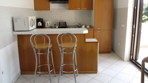Una cocina compacta con armarios de madera, un microondas, un tostador y dos taburetes de bar.