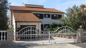 Una casa de dos pisos con techo de tejas, entrada con reja y un pequeño jardín.