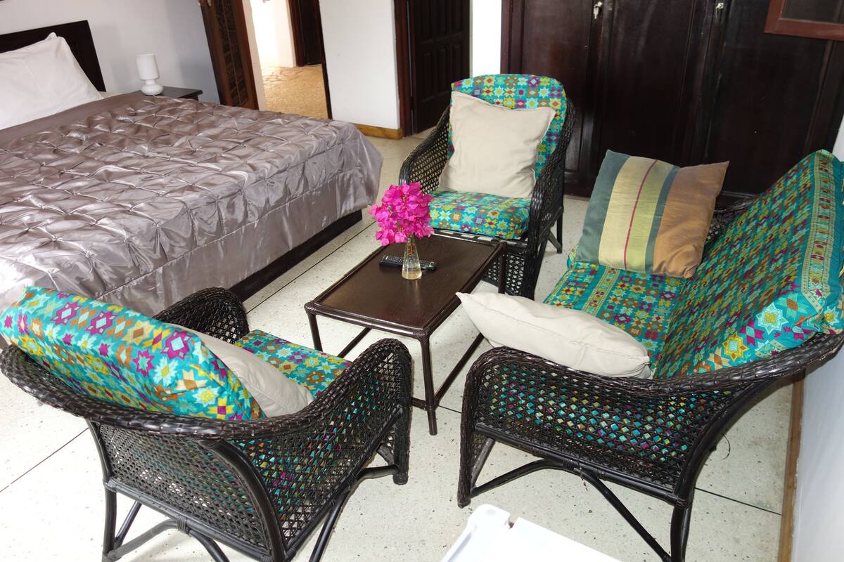 A bedroom with a bed, two wicker chairs, a small table, and a vase with flowers.