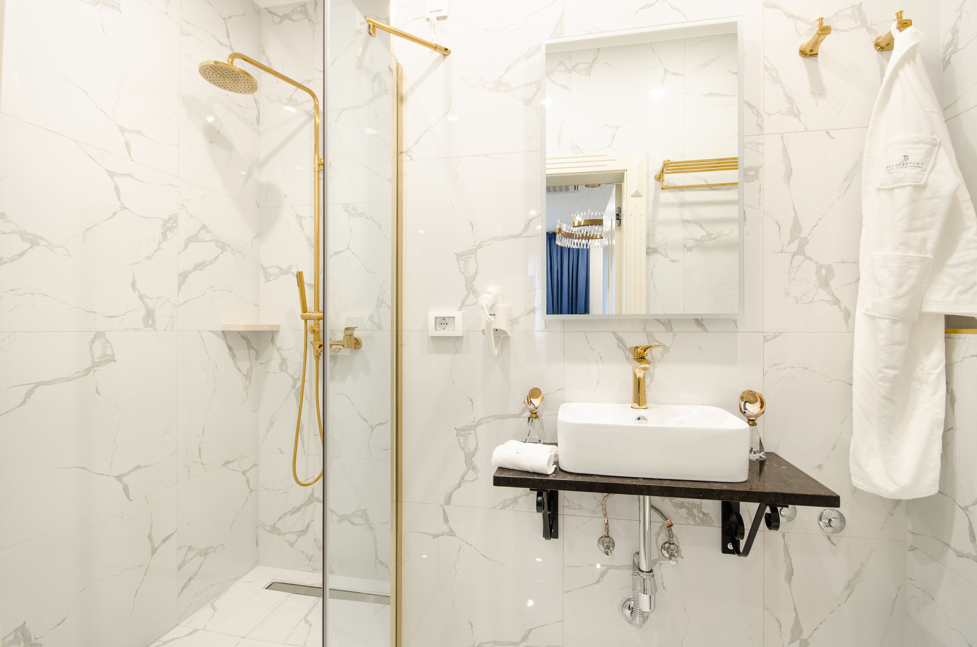 A modern bathroom with a glass-enclosed shower, a white sink with gold fixtures, and marble walls.