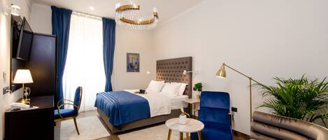 A modern hotel room with a bed, a desk, a chair, a sofa, and a potted plant.