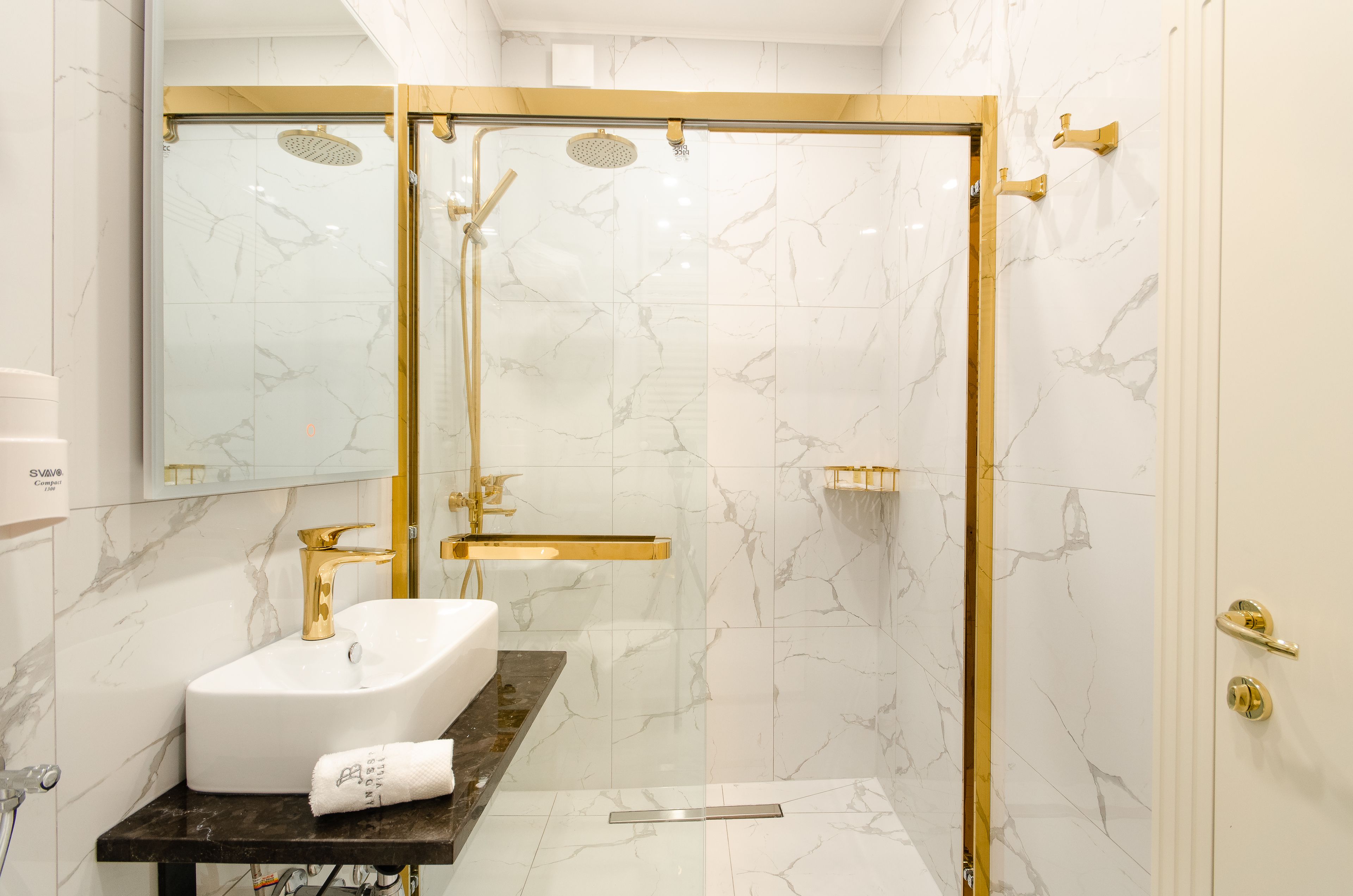 A modern bathroom with a white marble sink, gold fixtures, and a glass-enclosed shower.