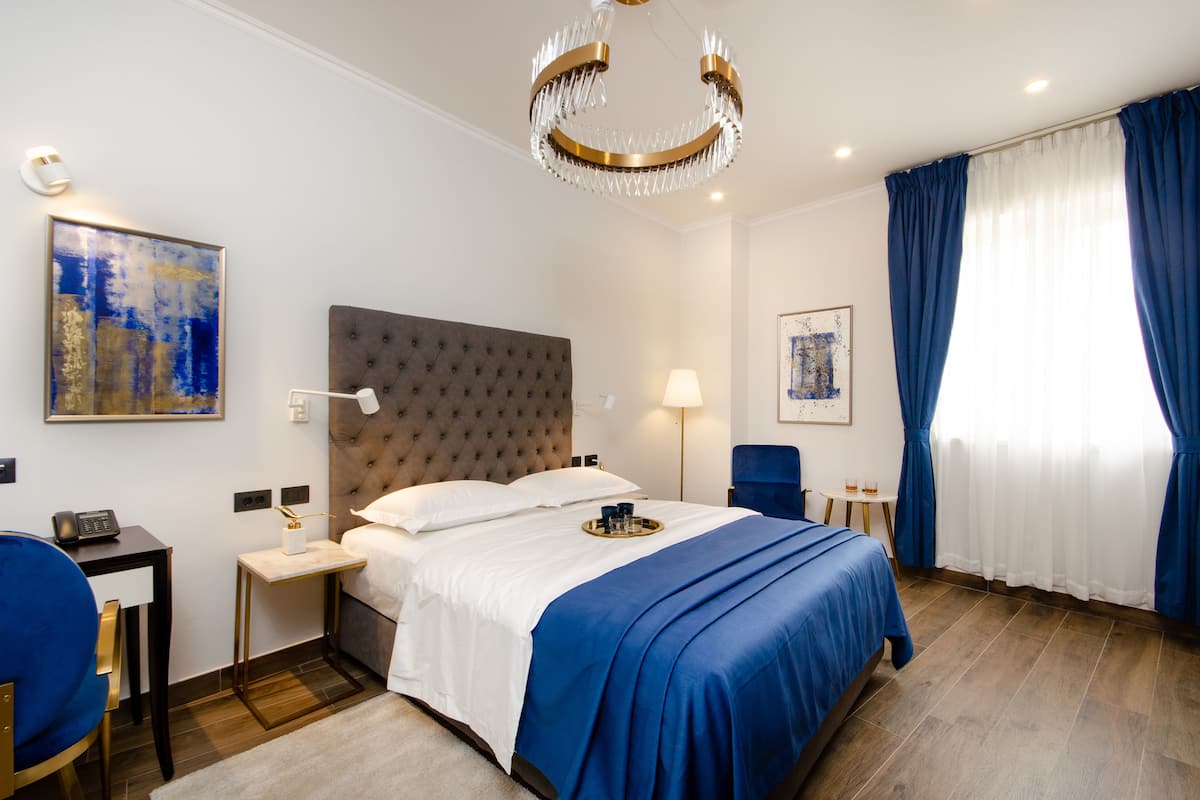 Habitación de hotel con una cama grande, un escritorio, una silla, una araña y obras de arte en las paredes.