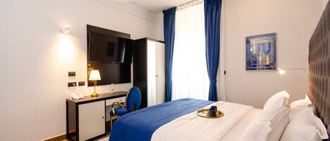 Una camera d'albergo moderna con un letto, una scrivania, una sedia, una televisione e una finestra con tende.