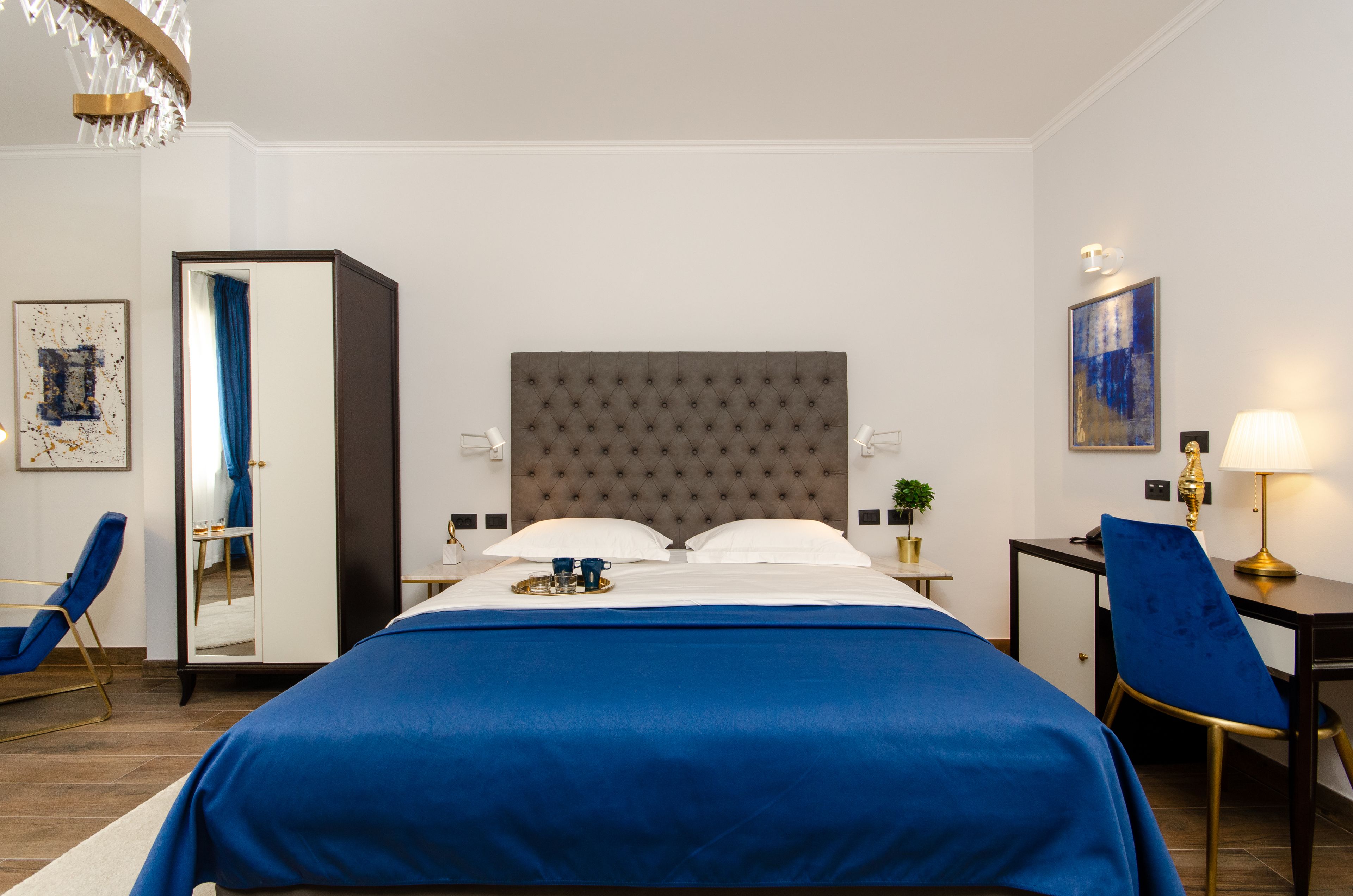 A hotel room with a large bed, a desk, a chair, a mirror, and a painting on the wall.