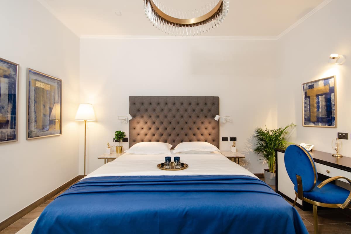 Una habitación de hotel con una cama grande, un escritorio, una silla, una lámpara y obras de arte en las paredes.