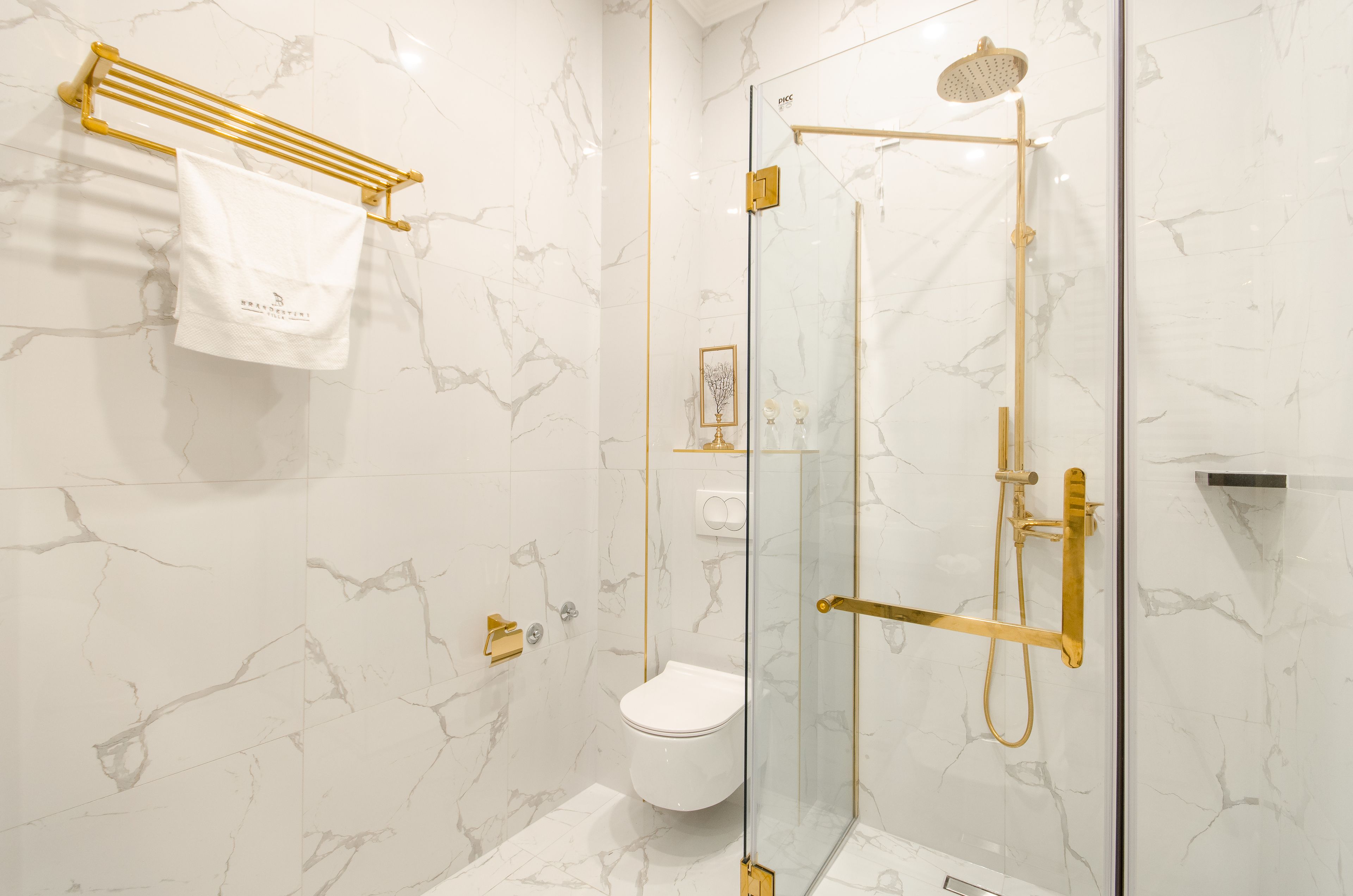 Un baño moderno con ducha de vidrio, inodoro blanco y toallero dorado.