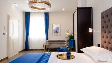 A modern hotel room with a large bed, a blue accent wall, a chandelier, a sofa, and a dining table with a tray.