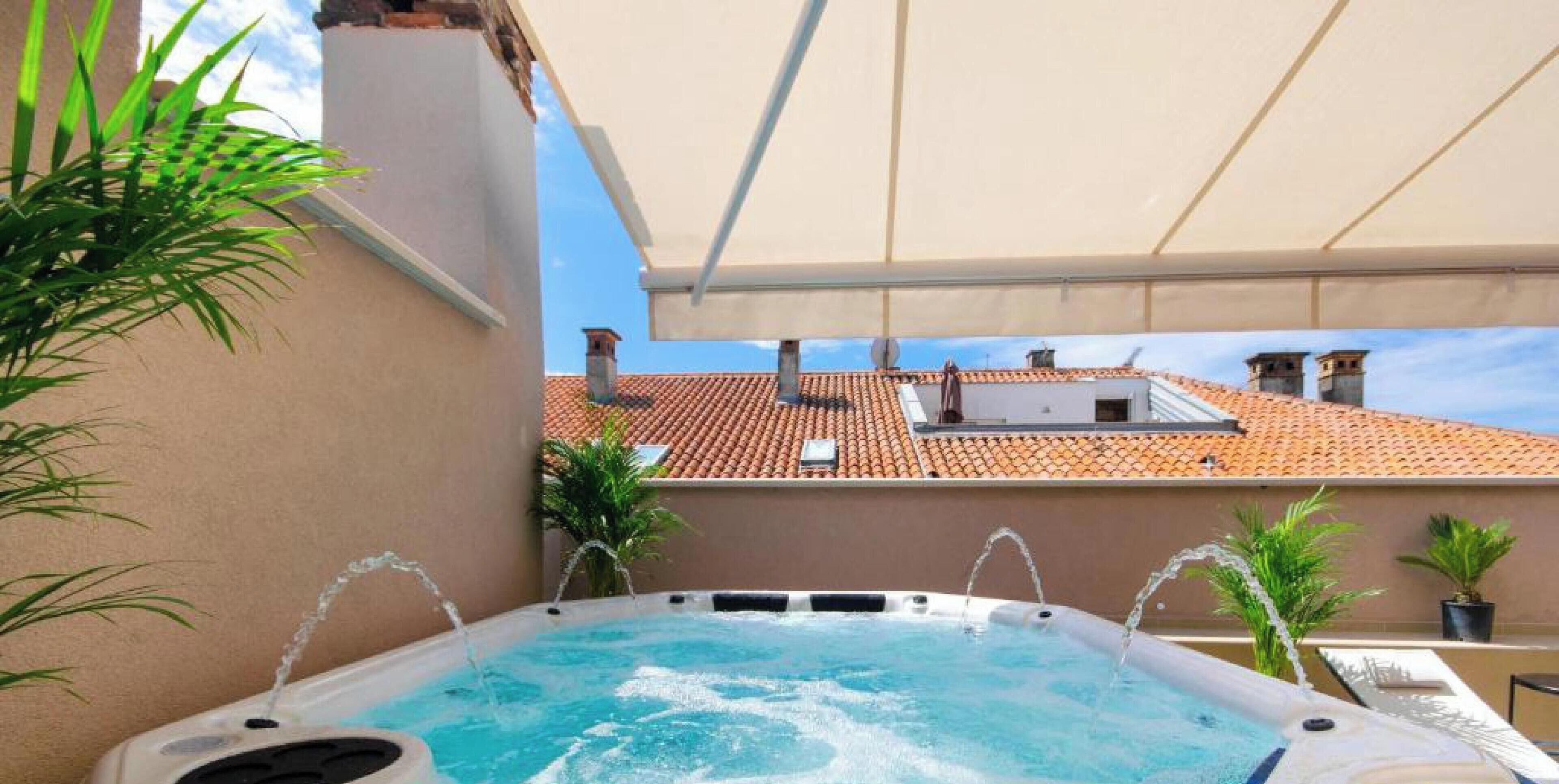 Una piscina en la azotea con hidromasajes, rodeada de macetas con plantas y un dosel blanco.