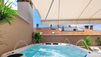 Una piscina en la azotea con hidromasajes, rodeada de macetas con plantas y un dosel blanco.
