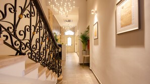 Una escalera con barandillas negras ornamentadas, un candelabro y un pasillo que conduce a una puerta.