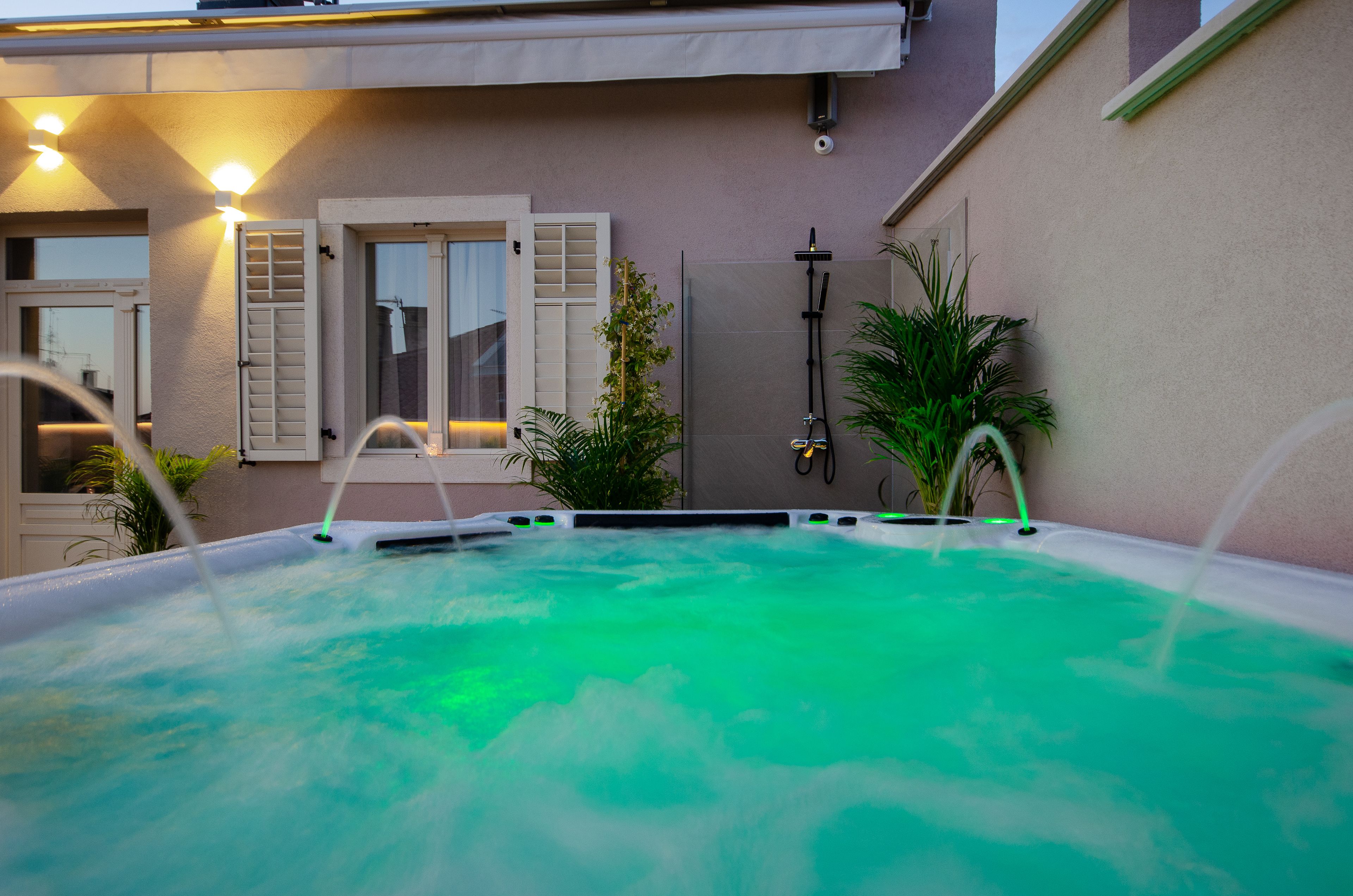 A hot tub with a view of a house with a balcony, a door, and a wall-mounted heater.