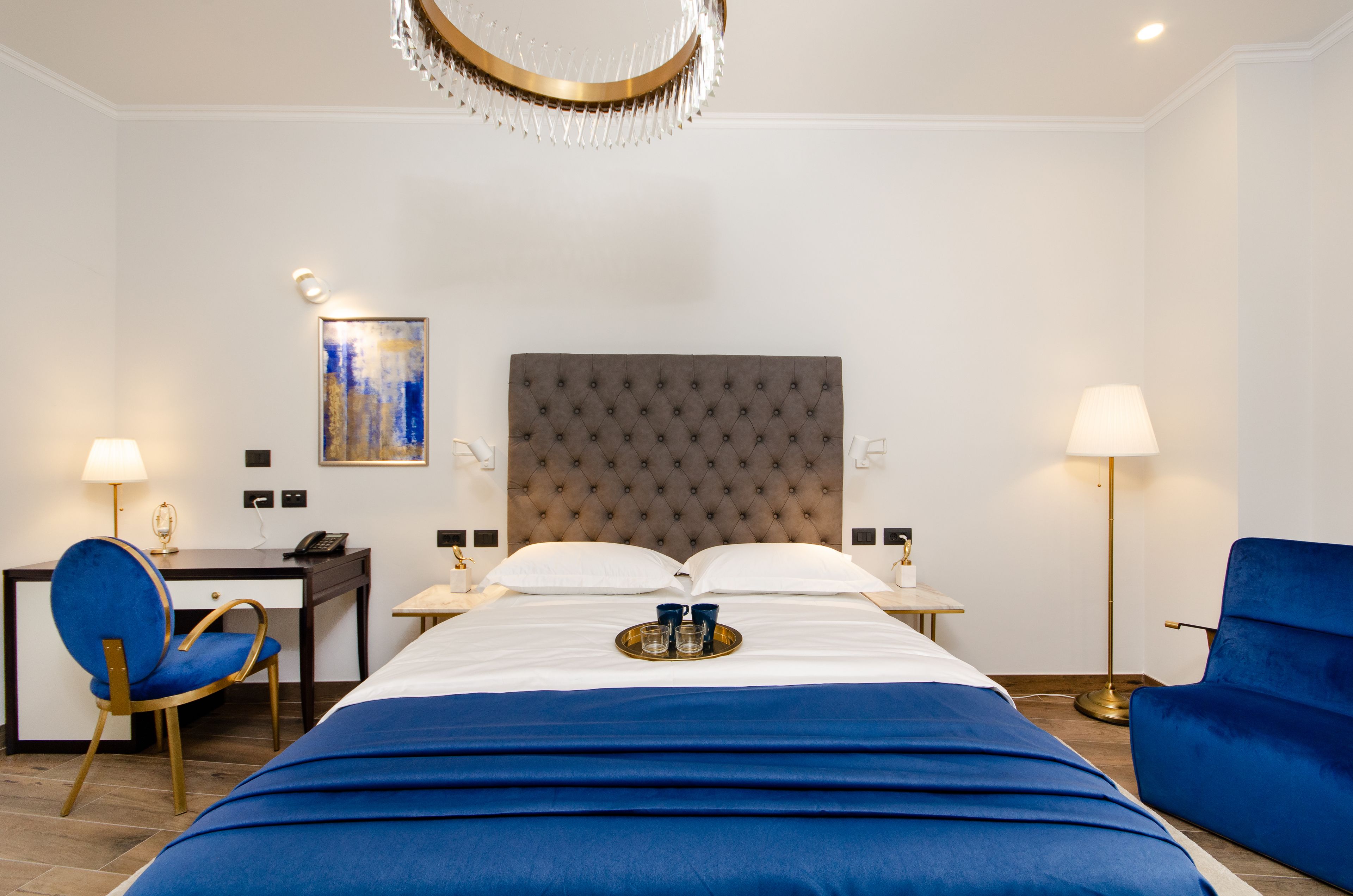 Une chambre d’hôtel avec un grand lit, un bureau avec une chaise, une lampe de bureau, une lampe sur pied et un tableau au mur.