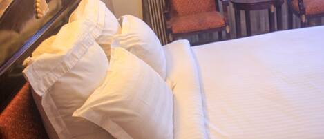 A hotel room with a bed, pillows, a wooden headboard, a small table, and two chairs.