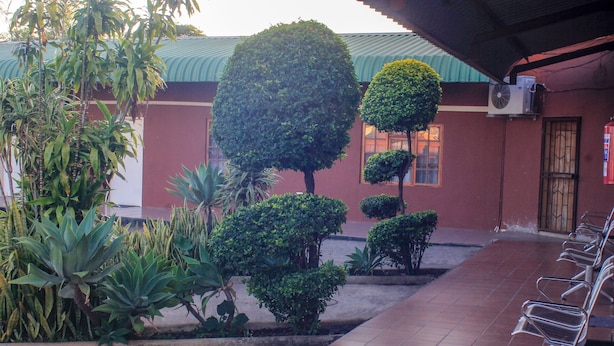 A courtyard with neatly trimmed bushes, a tiled floor, and a row of metal chairs. - Golden Pillow Lodge Monze (Monze)