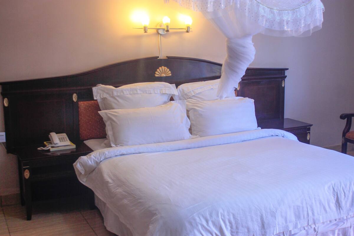 A neatly made bed with white linens, a bedside telephone, and a wall-mounted light fixture.