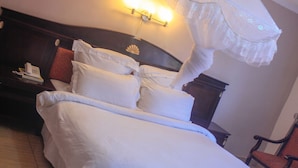 A neatly made bed with white linens, a bedside table with a telephone, and a chair in a hotel room. - Golden Pillow Lodge Monze (Monze)