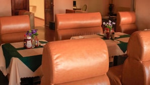 A dining area with leather chairs and tables, a vase with flowers, and condiments on the table. - Golden Pillow Lodge Monze (Monze)