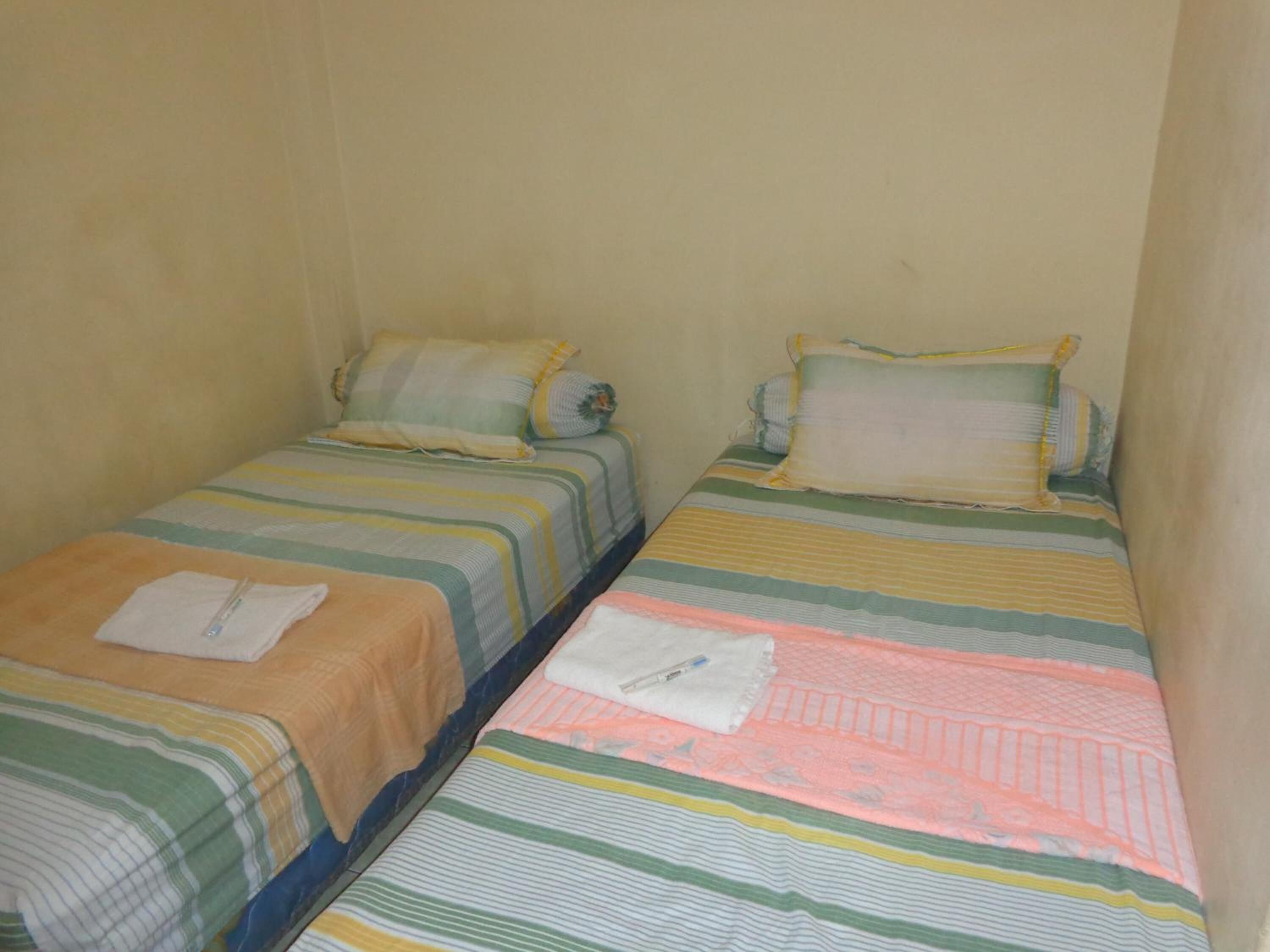 Dos camas individuales con ropa de cama a rayas en una habitación pequeña con paredes lisas.