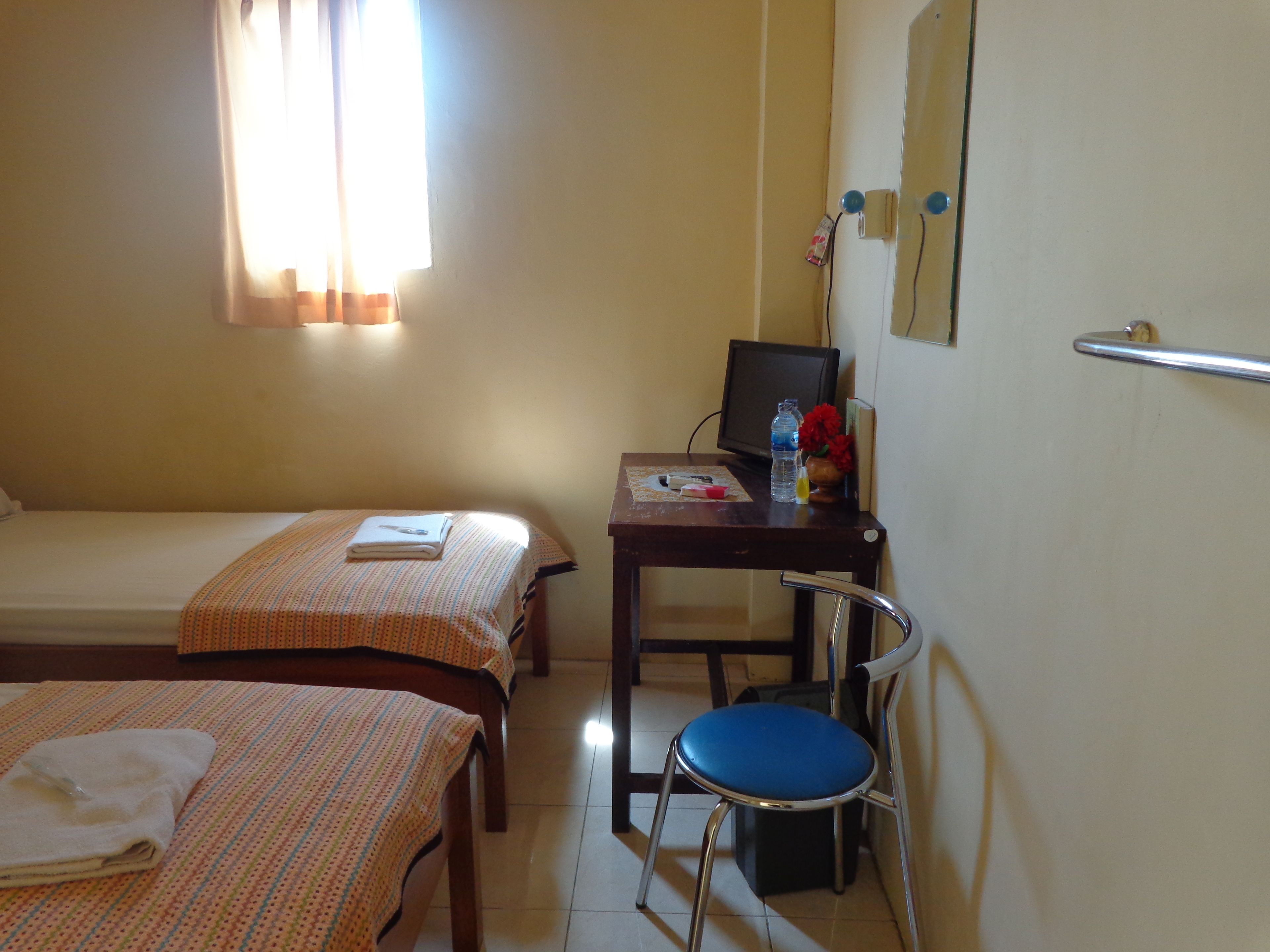 Una habitación de hotel con dos camas individuales, un escritorio con una computadora, una silla y una pequeña mesa con un florero.