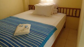 A single bed with a blue-striped bedspread and white pillows, a folded towel, and a wooden headboard. - Hotel Musafir Inn (Padang)