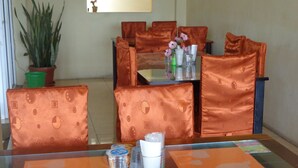 A dining area with a glass table, orange cushioned chairs, and a potted plant. - Hotel Musafir Inn (Padang)