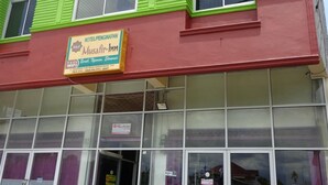 A hotel with a green and red facade, large windows, and a sign advertising free WiFi. - Hotel Musafir Inn (Padang)