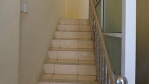 A staircase with beige tiles and a metal handrail, leading to a room with a greenish wall and a white door. - Hotel Musafir Inn (Padang)