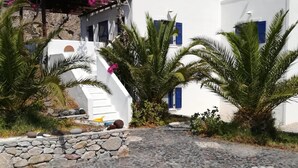 Un edificio blanco con contraventanas azules, rodeado de palmeras y buganvillas rosadas.
