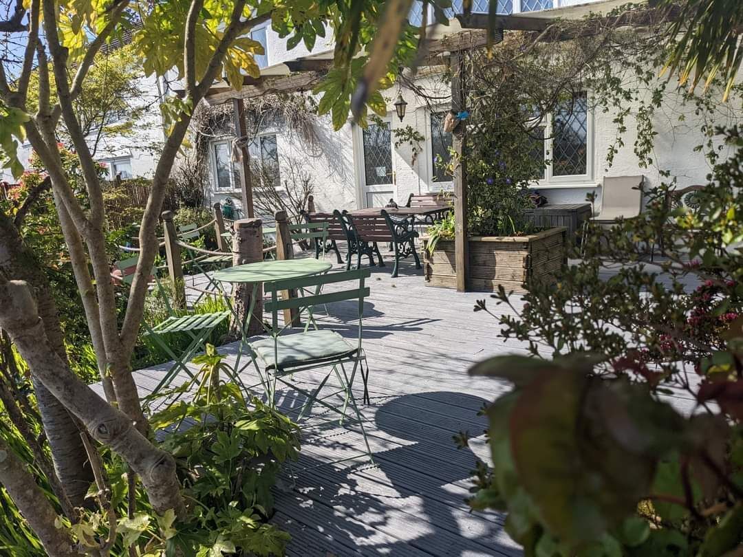 An outdoor patio with wooden flooring, green and brown furniture, and a pergola with climbing plants.