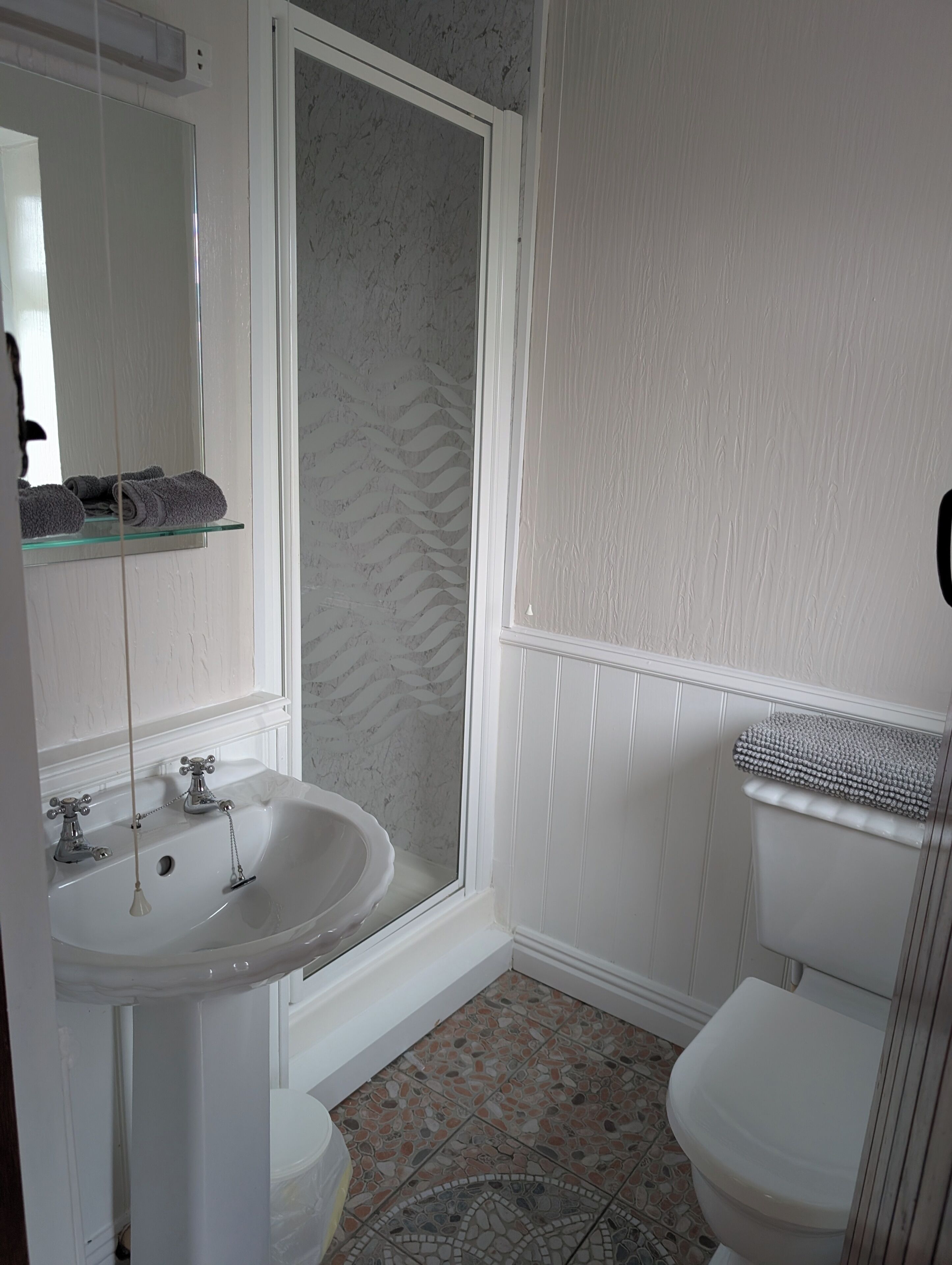 Une salle de bain avec un lavabo blanc, un miroir, une douche et des toilettes.