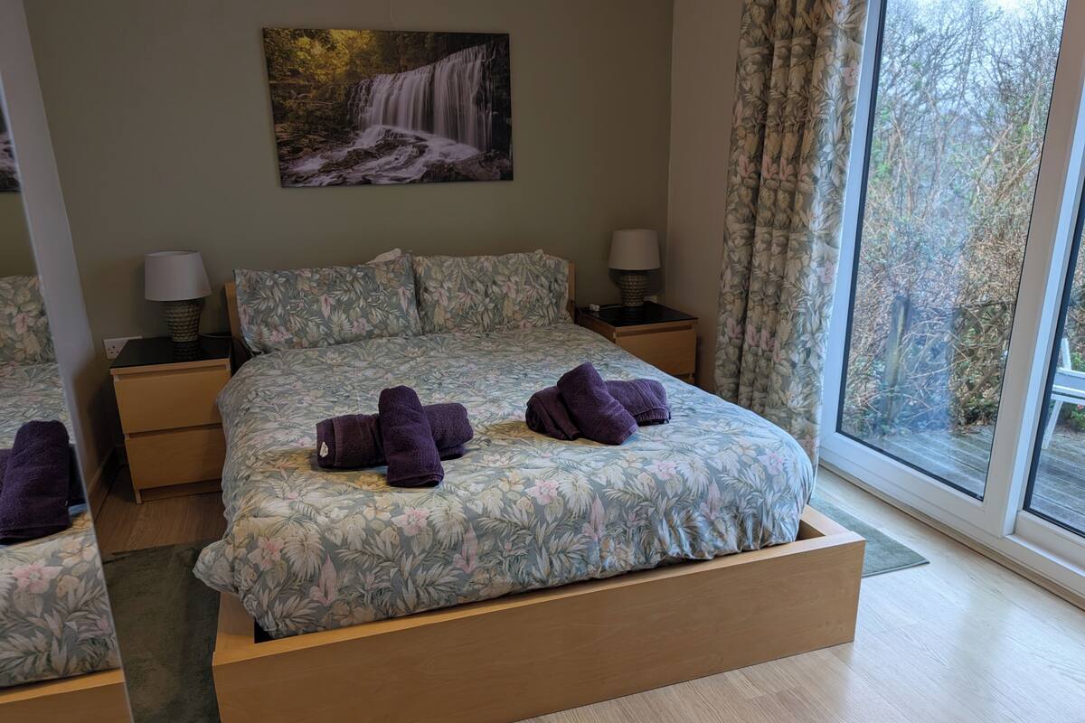 Une chambre à coucher avec un grand lit, deux tables de chevet, une fenêtre avec des rideaux et un tableau au mur.