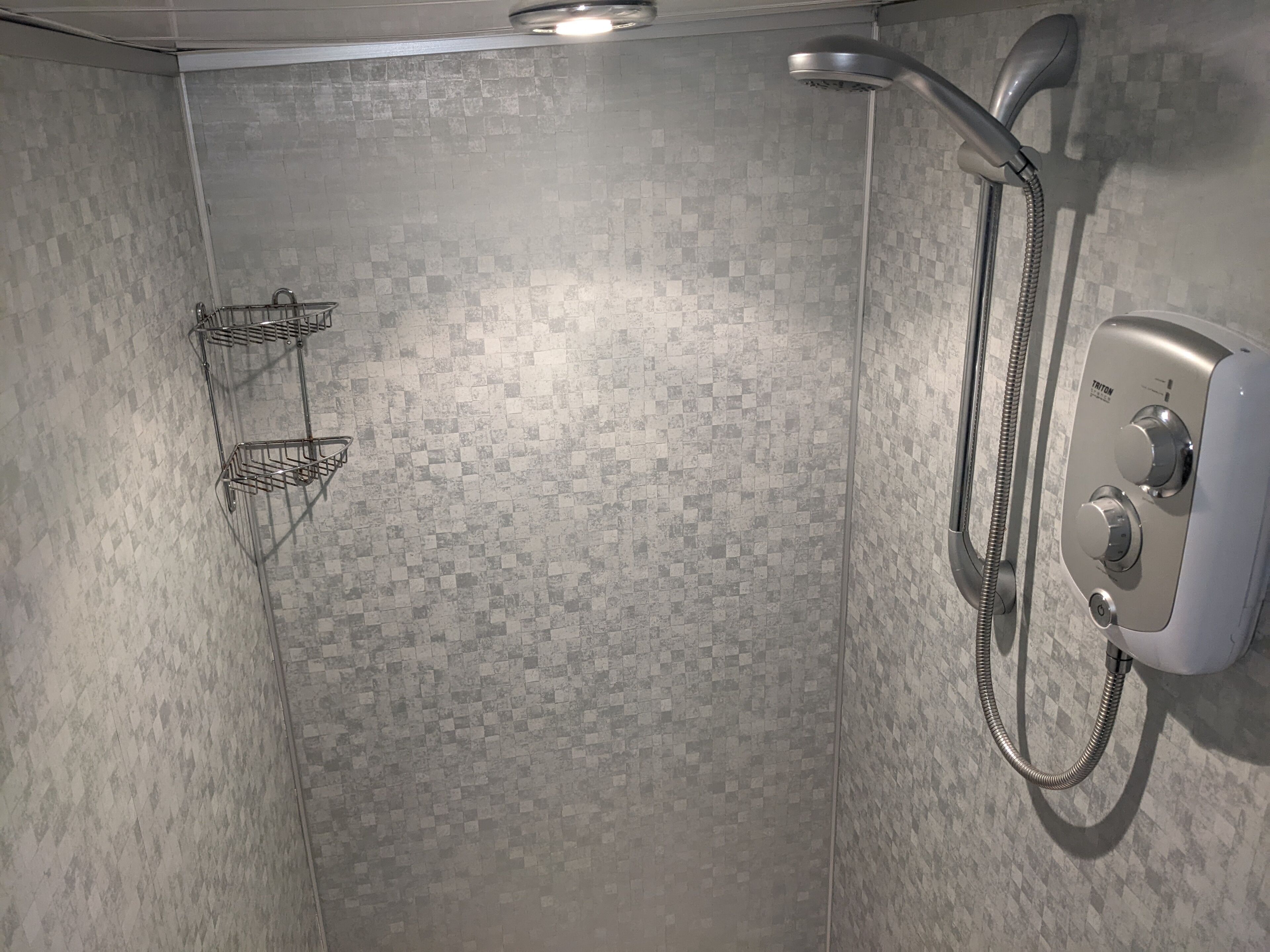 A shower with a handheld showerhead and a wall-mounted control panel.
