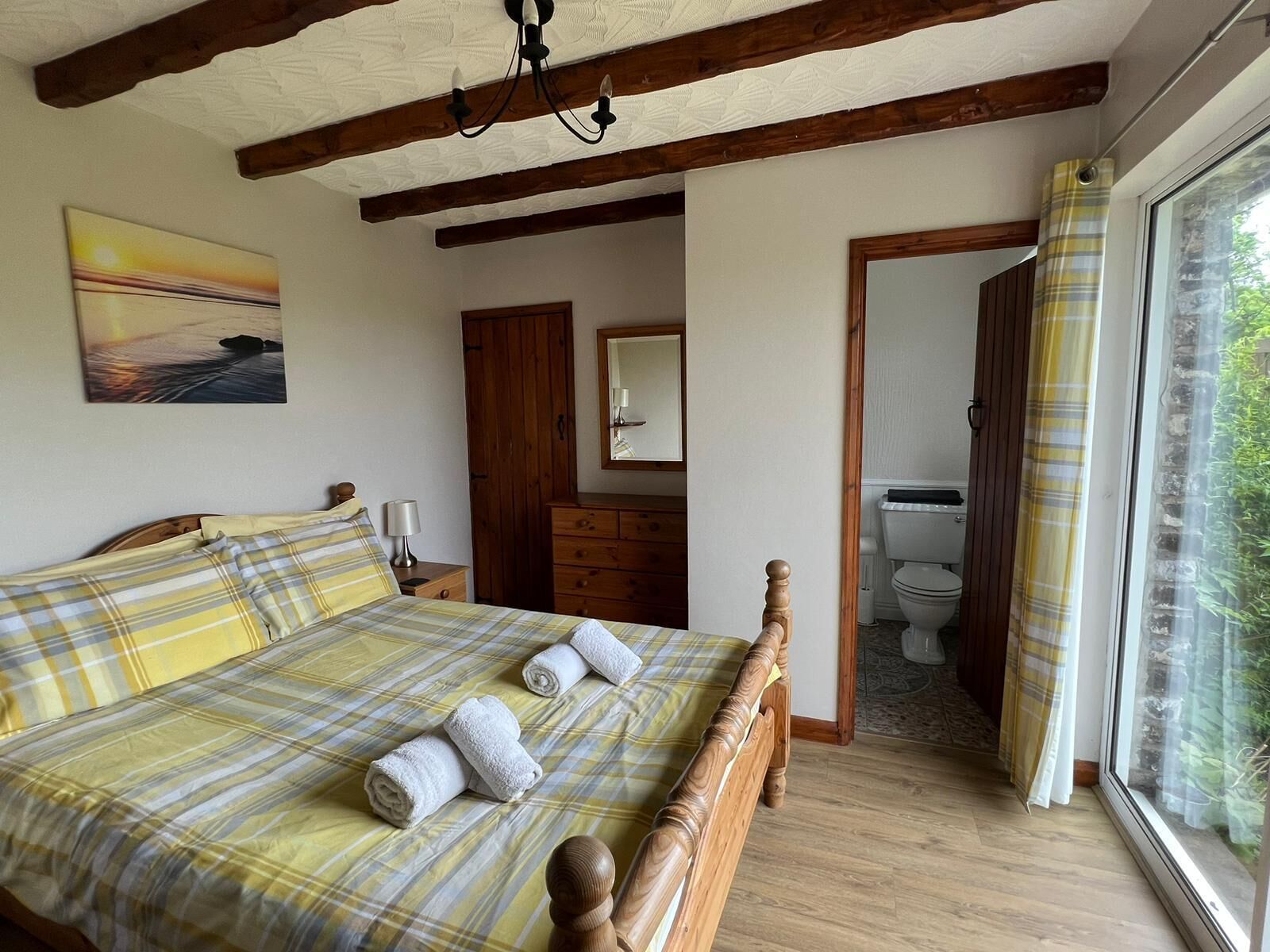 Ein Schlafzimmer mit einem hölzernen Bett, einem Nachttisch, einer Kommode und einem großen Fenster mit Vorhängen.