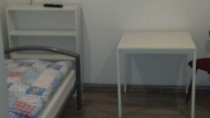 A bedroom with a bed, a bedside table, a TV mounted on the wall, and a small white table. - Gästehaus Willis (Goslar)