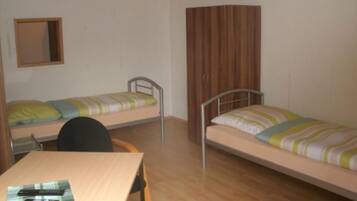 Ein Schlafsaalzimmer mit zwei Einzelbetten, einem Holztisch, einem Stuhl und einem Kleiderschrank.